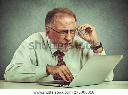 Closeup portrait senior elderly mature business man with glasses having eyesight problems confused with laptop software isolated gray background. Age related changes. technology and senior people