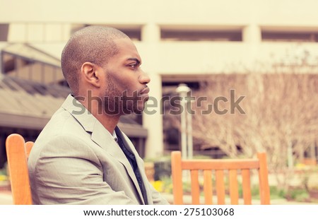 side profile stressed young businessman sitting outside corporate office looking away unhappy. Negative human emotion facial expression feelings.