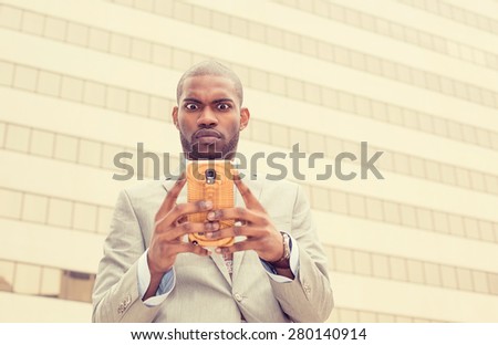 Confused surprised unhappy young man using texting on smart phone reading news message email isolated outside on corporate city building windows background