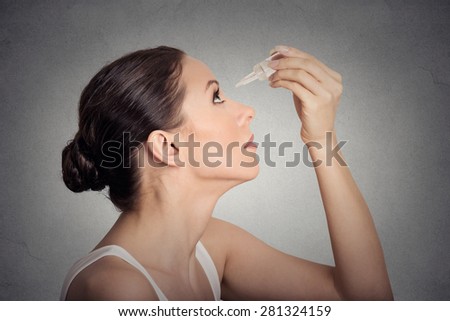 Side profile young woman applying eye drops isolated on gray wall background