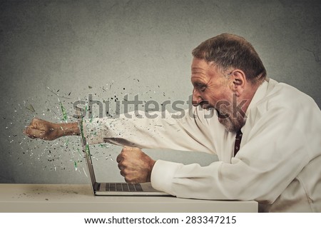 furious senior businessman throws punch into computer screaming isolated grey office wall background. Negative human emotions, facial expressions, feelings, aggression, anger management issues concept