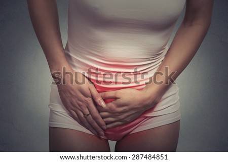Close up of a woman in pain with hands holding her crotch lower abdomen colored in red inflammation isolated on gray wall background