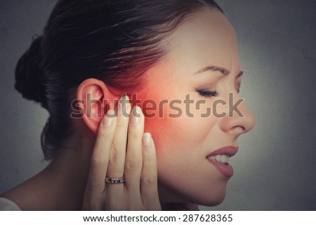 Tinnitus. Closeup up side profile sick female having ear pain touching her painful head isolated on gray wall background