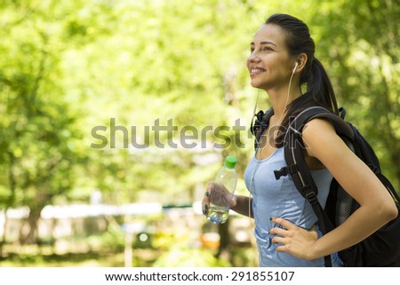Attractive female hiker with backpack walking and smiling on a country forest trail landscape