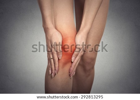 Closeup tendon knee joint problems on woman leg indicated with red spot isolated on gray background. Joint inflammation concept.