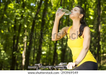 Happy mountain forest cyclist young woman in yellow t-shirt outdoors drinking water enjoying summer day fresh air