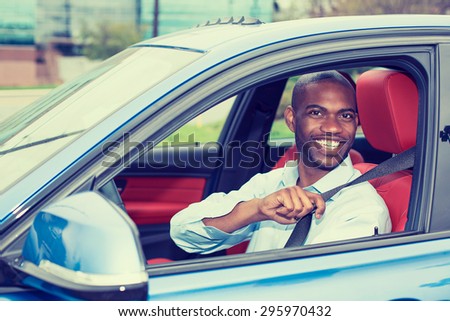 Car driver young man wearing safety belt driving new blue car  in summer. Happy male looking at camera.