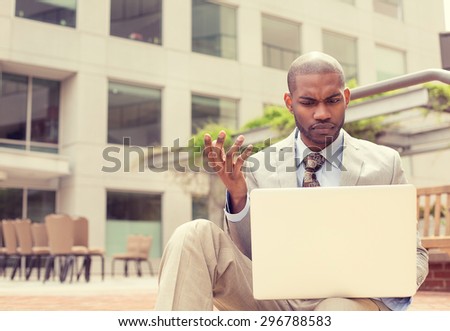 Portrait of business man in blue shirt sitting outside office looking at laptop and being frustrated about computer or software crash