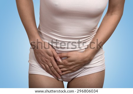 Close up cropped image of a young sick woman with hands holding pressing her crotch lower abdomen isolated on blue background. Gynecology problem treatment healthcare concept
