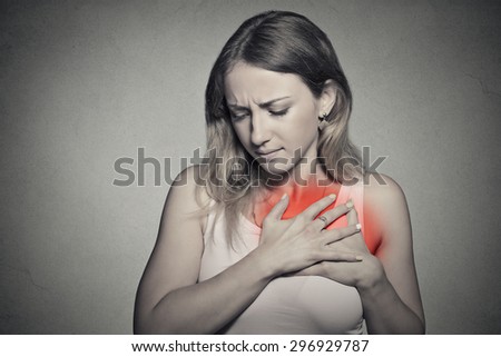 sick woman with heart attack, pain, health problem holding touching her chest colored in red with hands isolated on gray wall background. Human face expression