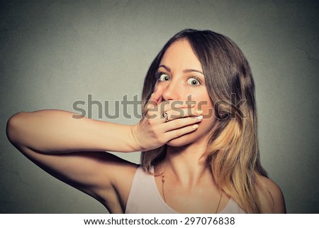 Portrait of scared young woman covering with hands her mouth isolated on gray wall background