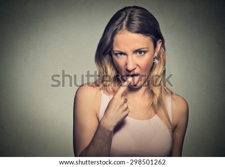 Closeup portrait young woman, annoyed, frustrated fed up sticking her finger in her throat showing she is about to throw up isolated on gray wall background