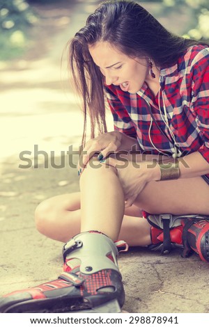 in-line skating injured young woman suffering from pain sitting on the ground touching painful knee waiting in need for medical help outdoors on summer day