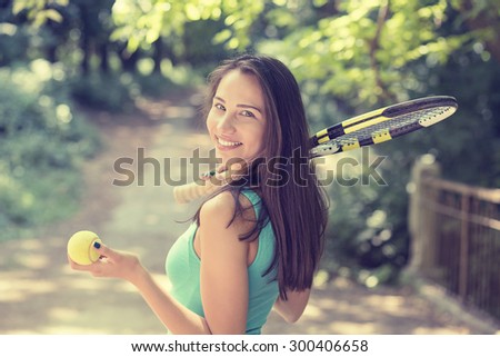 Portrait successful happy young sports woman with racket walking in park on summer sunny day. Healthy lifestyle wellness concept. Isolated on green trees background