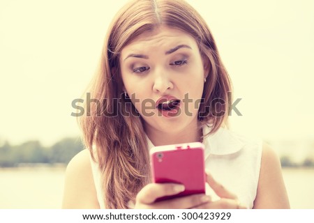 portrait anxious young girl woman looking at phone reading seeing bad news or photos with disgusting emotion on her face isolated outside outdoors background. Human emotion, reaction, expression