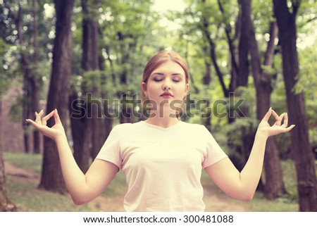 Portrait beautiful young woman meditating with eyes closed outdoors in park forest on summer spring day