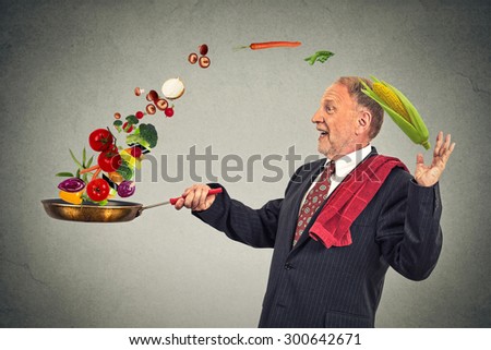 Side profile mature happy businessman cooking vegetables with a pan isolated on grey wall background. Positive face expression emotion.
