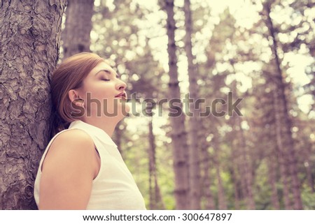 Side profile portrait relaxing young woman enjoying summer day in forest taking deep breath leaning on a tree