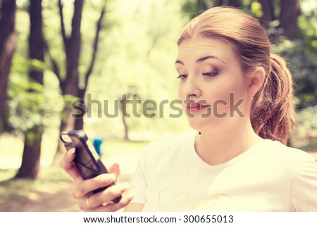 Closeup portrait upset skeptical unhappy serious woman talking texting on phone displeased with conversation isolated park trees outdoors background. Negative human emotion face expression feeling