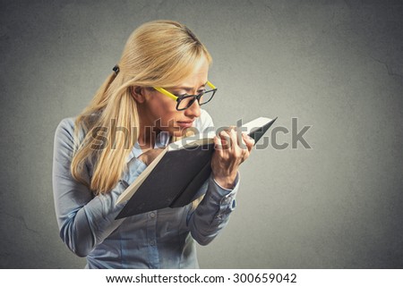 Closeup portrait young woman with eye glasses trying read book, having difficulties seeing text, has bad vision sight problems isolated gray background. Face expression reaction health eyesight issues