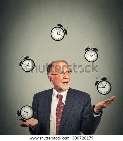 Portrait senior business man in suit juggling multiple alarm clocks isolated on gray office wall background. Timing concept