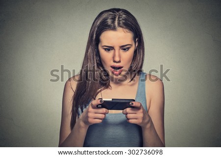 Closeup portrait anxious young girl looking at phone seeing bad news or photos with disgusting emotion on her face isolated on gray wall background. Human emotion, reaction, expression