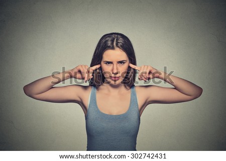 Closeup portrait young angry unhappy woman with closed ears looking at you annoyed by loud noise giving her headache ignoring isolated on gray wall background. Negative emotion perception attitude