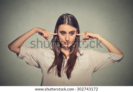 Closeup portrait young angry unhappy woman with closed ears looking away annoyed by loud noise giving her headache ignoring isolated on gray wall background. Negative emotion perception attitude