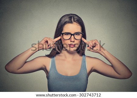 Portrait young angry unhappy woman with glasses plugging ears with fingers looking at you annoyed loud noise giving her headache ignoring isolated gray background. Negative emotion perception attitude