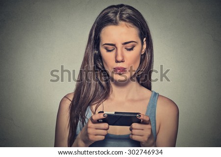 Portrait young angry woman unhappy, annoyed by something, someone on her cell phone texting, receiving bad sms text message news isolated gray wall background. Human face expression emotion reaction