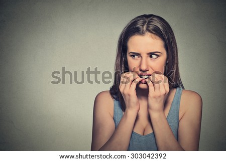Closeup portrait young unsure hesitant nervous woman biting her fingernails craving for something or anxious, isolated on gray wall background. Negative human emotions facial expression feeling
