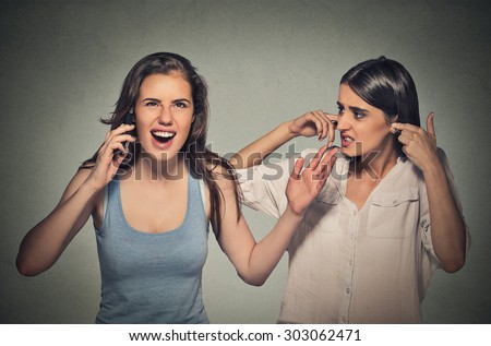 Portrait two women loud, obnoxious rude woman talking loudly on cell phone, girl next to her pissed off closes ears having headache Isolated gray background. Negative emotion facial expression feeling