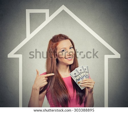 home, money, people concept. Smiling young successful happy business woman holding dollar cash money in hand over house and gray wall background