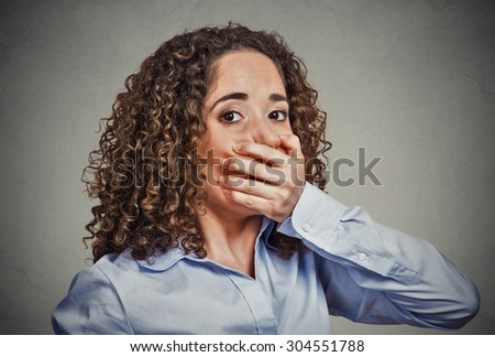 Portrait of scared young woman covering with hand her mouth isolated on gray wall background