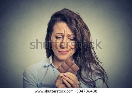 Portrait sad young woman tired of diet restrictions craving sweets chocolate isolated on gray wall background. Human face expression emotion. Nutrition concept. Feelings of guilt