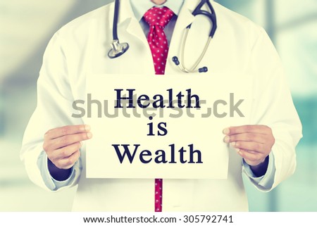 Closeup doctor hands holding white card sign with health is wealth text message isolated on hospital clinic office background. Retro instagram style filter image