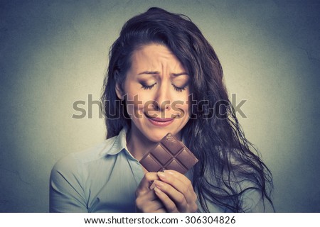 Portrait sad young woman tired of diet restrictions craving sweets chocolate isolated on gray wall background. Human face expression emotion. Nutrition concept. Feelings of guilt