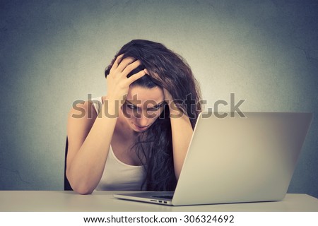 Too much work sleepy stressed young woman sitting at her desk in front of computer isolated on gray wall office background. Busy schedule in college, workplace, sleep deprivation concept