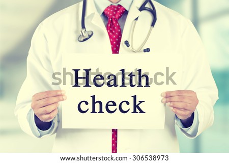 Closeup doctor hands holding white card sign with health check text message isolated on hospital clinic office background. Retro instagram style filter image