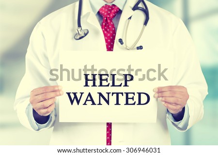 Closeup doctor hands holding white card sign with help wanted text message isolated on hospital clinic office background. Retro instagram style filter image