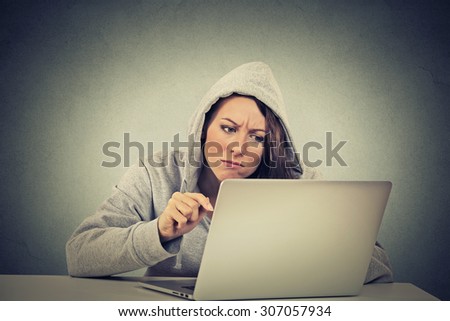 young stressed displeased worried woman sitting in front of laptop computer on gray wall background. Negative face expression emotion feelings problem perception