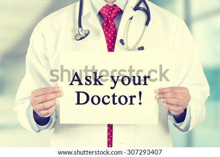 Closeup doctor hands holding white card sign with Ask your Doctor text message isolated on hospital clinic office background. Retro instagram style filter image. Healthcare concept