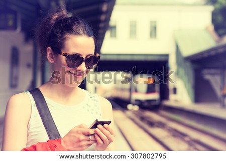 Young woman using her cell phone on subway platform, checking message sms e-mail or train schedule. Girl texting on smartphone