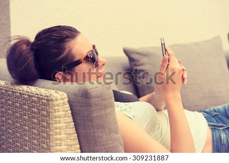 Happy young girl texting on the smart phone in a hotel restaurant terrace lounge