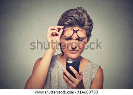 Closeup portrait headshot young woman with glasses having trouble seeing cell phone has vision problems. Bad text message. Negative human emotion facial expression perception. Confusing technology