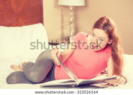 Surprised young woman reading magazine laying on a bed of a hotel room