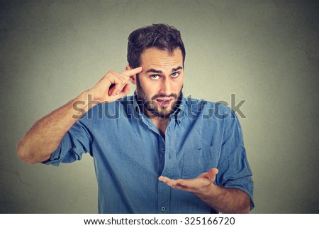 Closeup portrait of angry mad young man gesturing with his finger against temple asking are you crazy? Isolated on gray wall background. Negative emotions facial expression feeling body language
