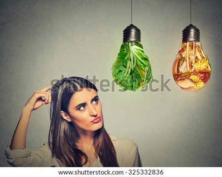 Portrait beautiful woman thinking looking up at junk food and green vegetables shaped as light bulb isolated on gray background. Diet choice right nutrition healthy lifestyle concept
