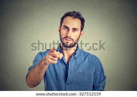 Portrait of a angry young man pointing finger at you camera gesture isolated on gray wall background