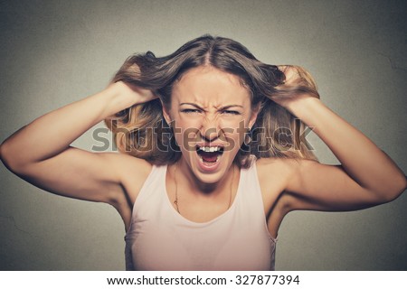 Closeup portrait stressed, frustrated angry woman pulling hair out yelling screaming temper tantrum isolated on grey wall background. Negative human emotion facial expression reaction attitude